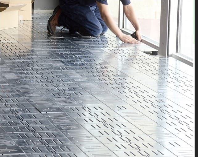 Technician installing modular raised-access floor panels during a control room build-out